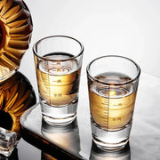 Two clear glass brandy cups with chinese measurement markings filled with golden liquid from a modern glass spirit set