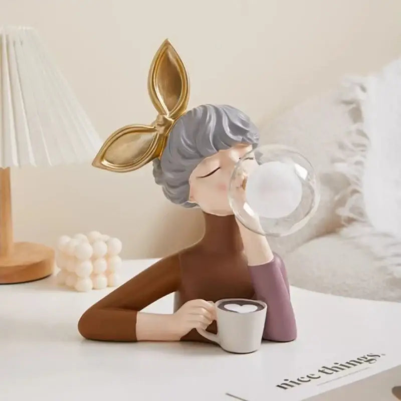 A modern gray and gold resin bubble girl statue with gray hair sipping from a white mug for bedroom decorbites decor