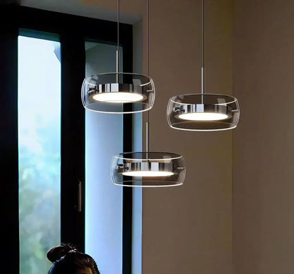 Three modern pendant lights with gray glass shades and plated detailing emitting warm glow for kitchen use