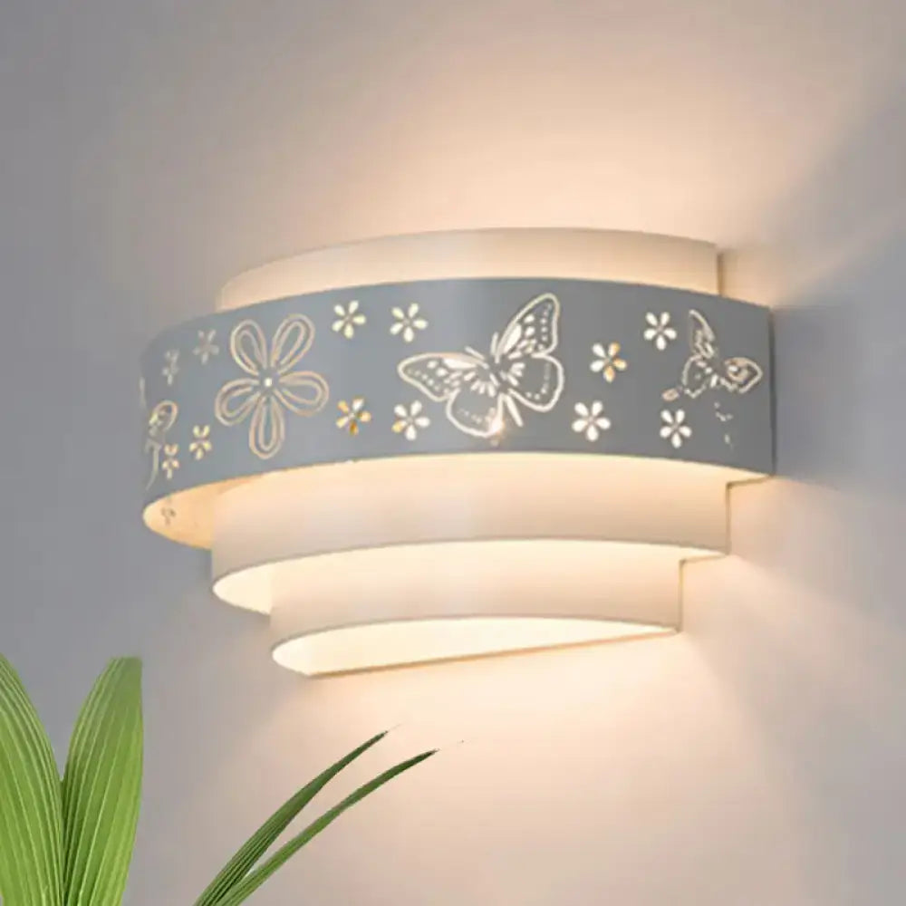 Modern gray metal wall sconce with etched pattern butterfly and flower cutouts emitting warm living room glow