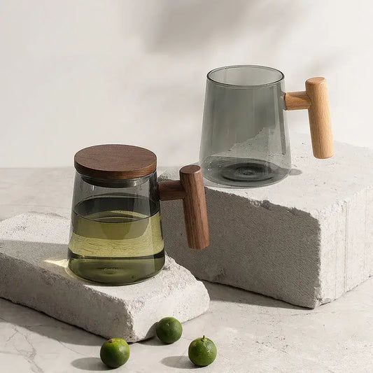 A sleek green and gray glass tea cup set with wood handle and dark wood lid displayed on concrete blocks