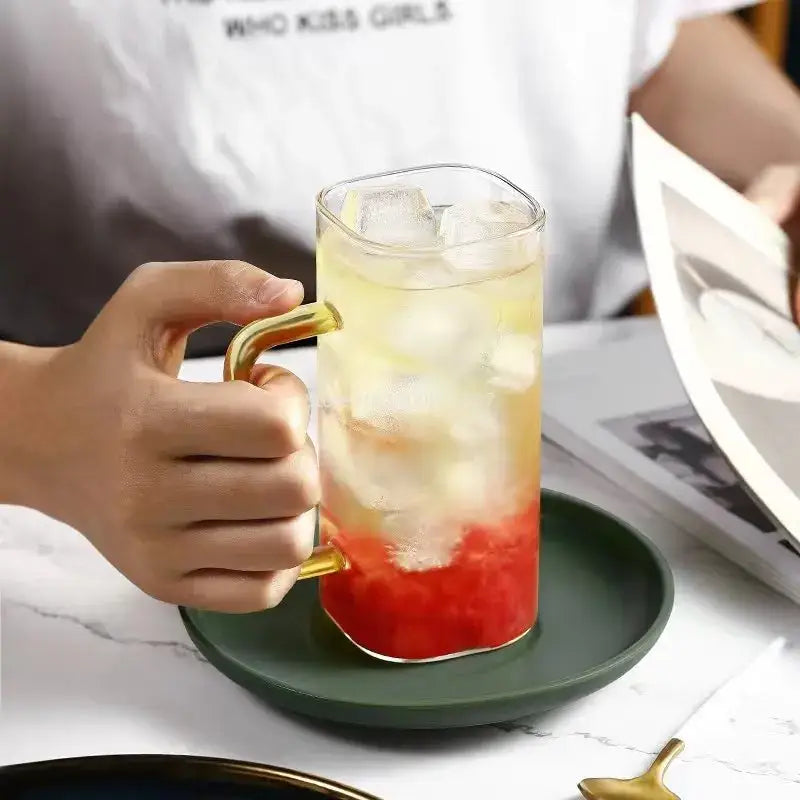 A clear square glass mug with a gold handle filled with ice and layered red and yellow liquid for drinking