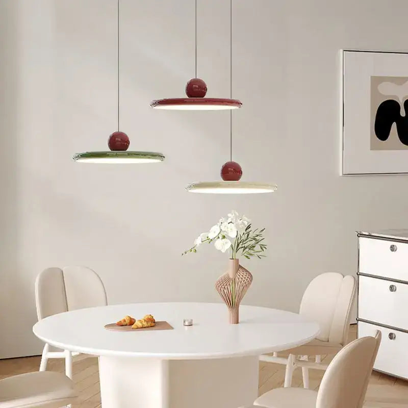 Three modern pendant lights with glossy red tops and cream wind saucer shades hang above a white dining table