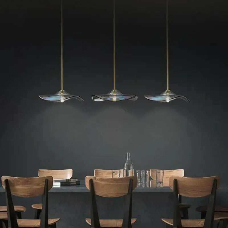 Three elegant translucent blue glass plated pendant lamps with gold fixtures hanging above a dining table