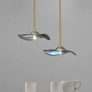 Two elegant iridescent glass plated pendant lamps with gold rods hang above white ceramic mugs in kitchen lighting