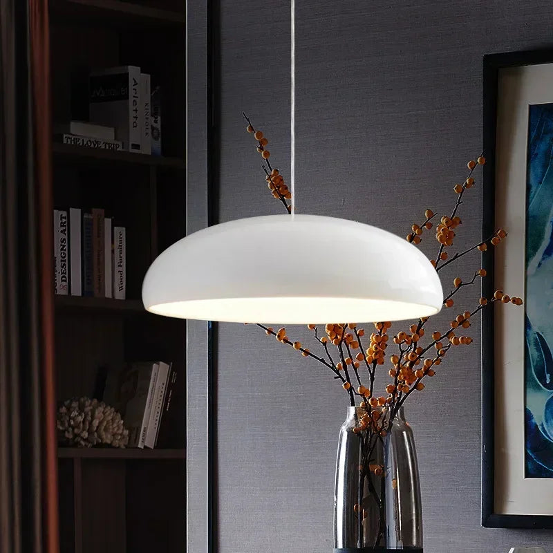 A sleek white modern pendant light with a round aluminum lampshade hanging over a dining table