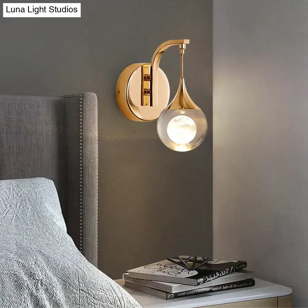 Gold-toned modern luxurious crystal led wall sconce with a curved arm and clear glass globe for bedroom lighting