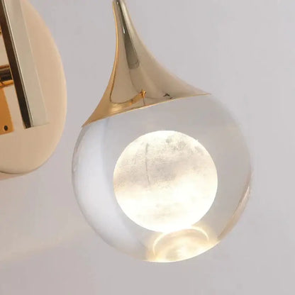 Modern luxurious crystal led wall sconce with gold curved metallic top and clear glass globe housing moon-shaped bulb