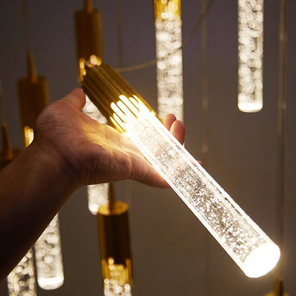 A hand holds a modern luxury crystal pendant lamp with gold metallic top and acrylic body emitting warm white light