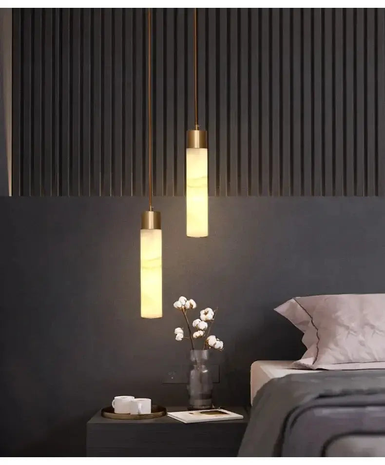 Two elegant gold-toned decorbites copper led pendant lights with warm cylindrical shades above a dark gray bedside table