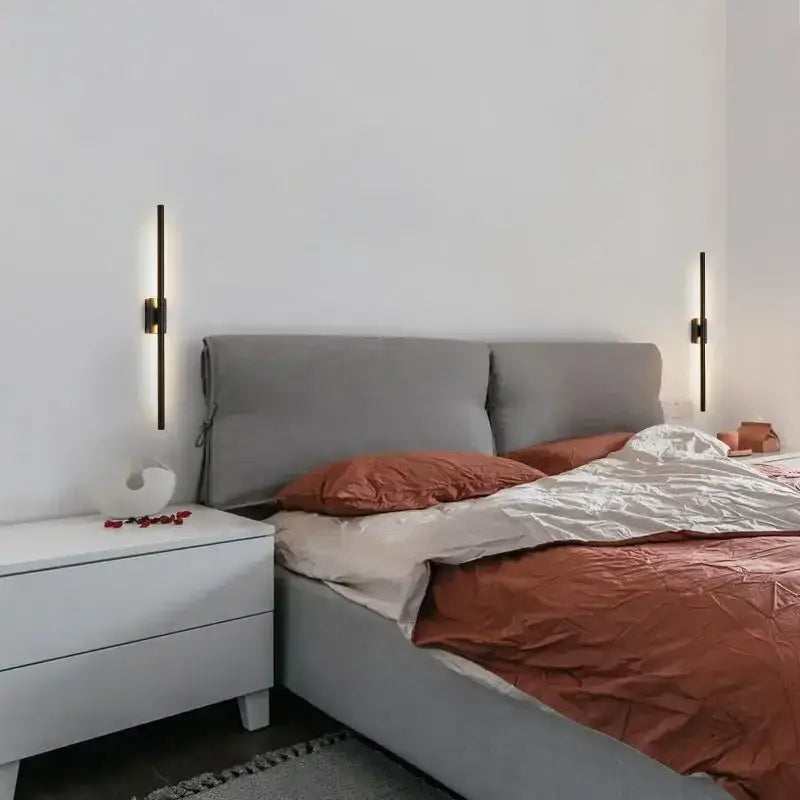 Modern matte black wall light with decorbites brass gold led accents above a gray tufted bed with rust bedding