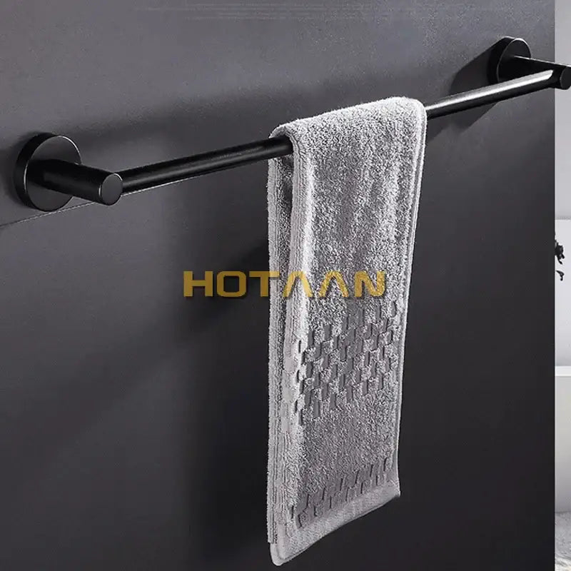 A soft gray towel hangs on a modern matte black wall mounted towel bar with wood accents in a bathroom