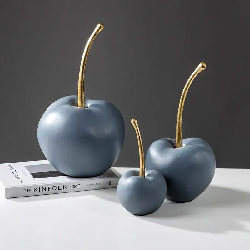 Three matte blue resin apple ornaments with gold stems arranged on a white surface for living room decor
