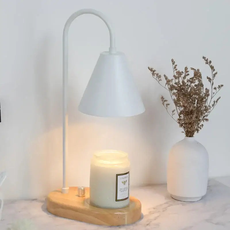 White metal electric candle lamp with curved neck and bell-shaped shade on light wood candle lamp warmer base
