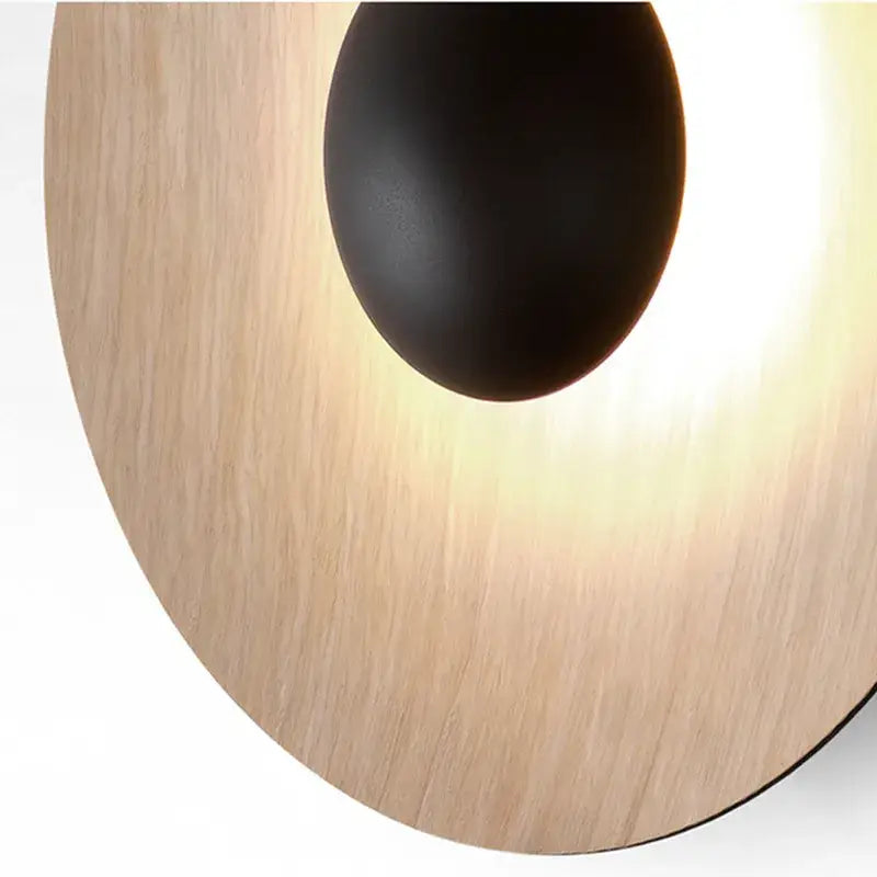 A modern matte white and brushed bronze ginger round wall lamp with a wooden base and oval black center for bedroom decorbites ginger round wall
