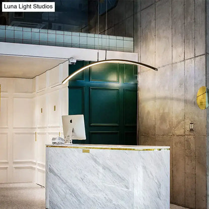 A sleek metallic arc shape led pendant light hangs above a marble dining room reception desk