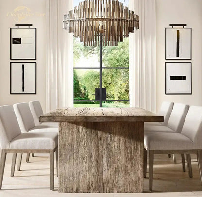 Rustic wooden dining table with thick textured surface and sturdy legs under modern metallic emile round led chandelier