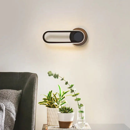 Modern minimalist black matte oval LED wall sconce with brass accents featuring a sleek design for natural colors
