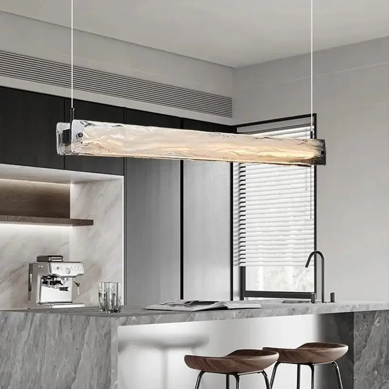 A modern minimalist cloud fog glass pendant light with textured translucent body and metallic ends above kitchen counter
