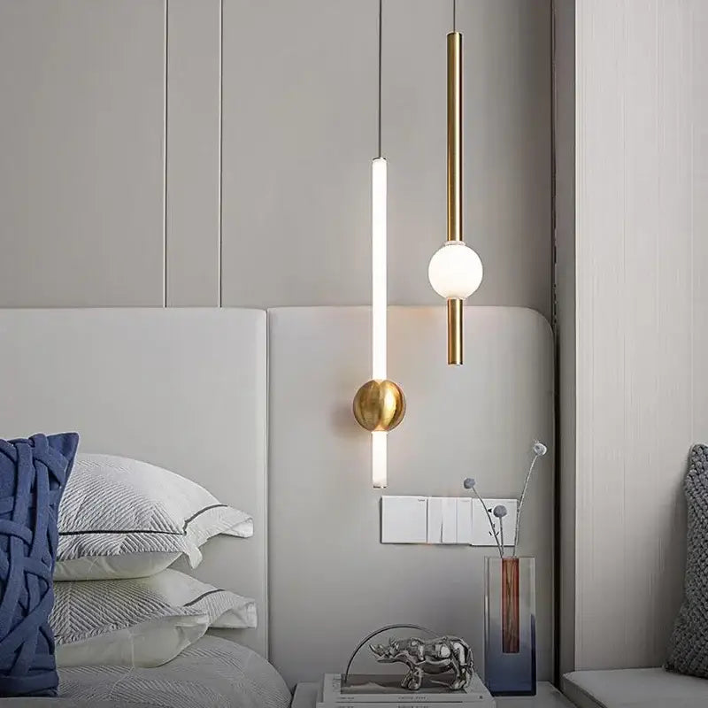 Modern minimalist gold-toned glass rod pendant light with cylindrical and spherical elements above a bed