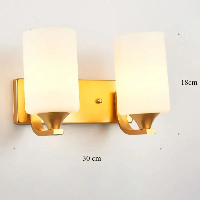 Modern minimalist wall lamp with gold finish and two cylindrical frosted glass shades for bedroom use