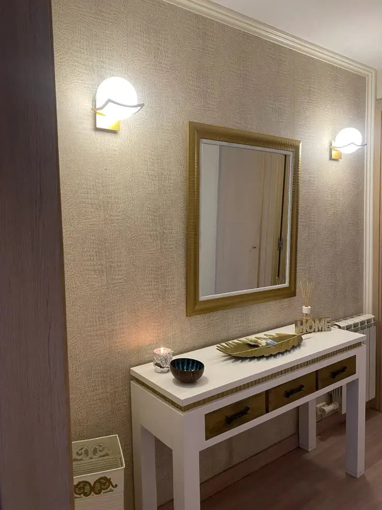 Gold-framed rectangular mirror with ornate detailing paired with modern minimalist glass shade gold wall lamp for bedroom
