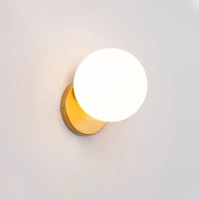 Modern minimalist wall lamp with gold-toned spherical glass shade and frosted globe for bedroom lighting