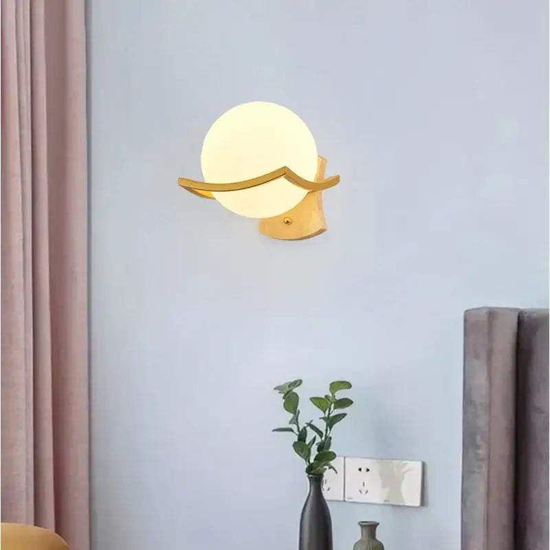 Modern minimalist wall lamp with gold-toned curved arms and a frosted white glass shade for bedroom use