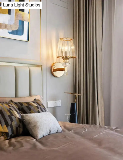 Modern minimalist wall sconce in gold tone with crystal-encrusted base and tiered translucent glass shade for bedroom