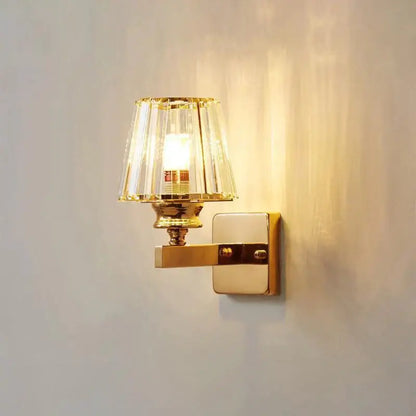 Modern minimalist wall lamp with gold-toned polished brass finish and faceted crystal shade for bedroom lighting