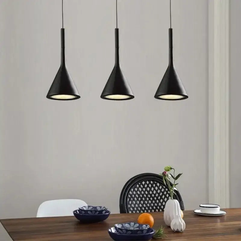 Three sleek black metal pendant lights hang above a wooden dining table in a modern minimalist kitchen setting