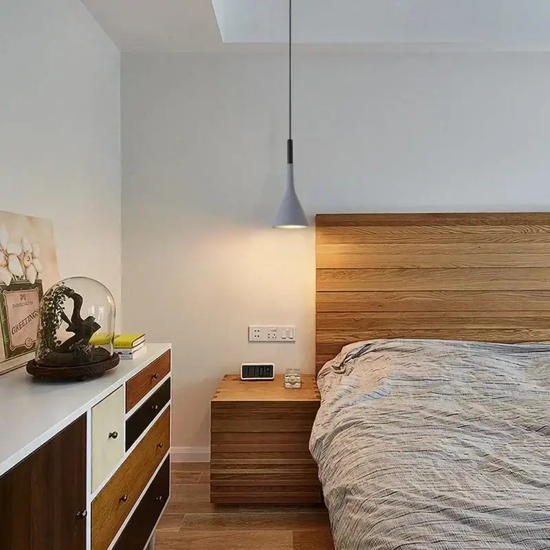 Modern nordic pendant light with sleek gray conical shade and black metal cord hanging above the bed