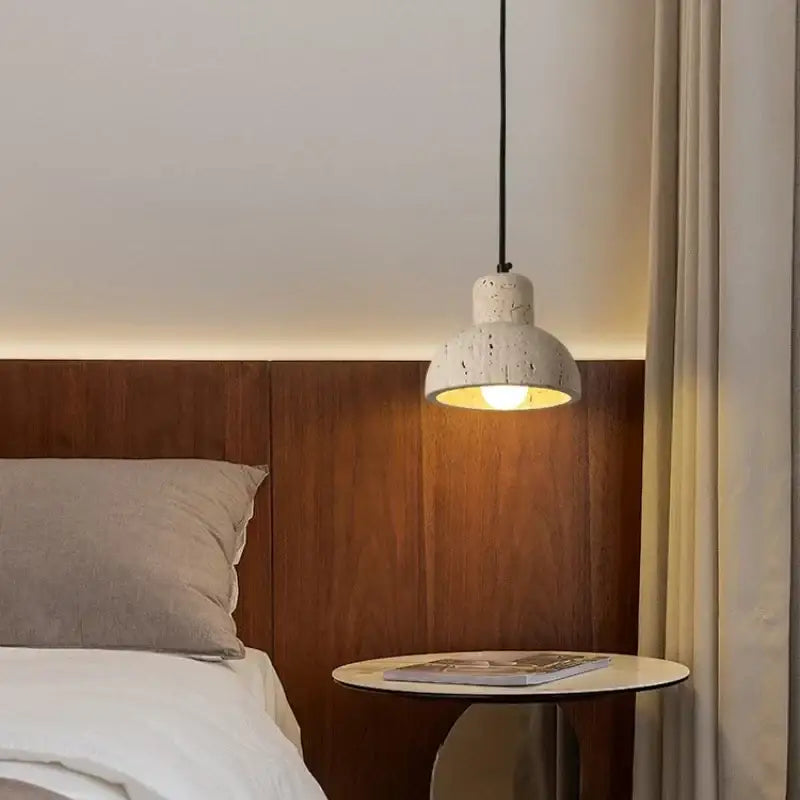 Modern off white cave stone led pendant light with white speckled concrete shade and black cord above bedside table