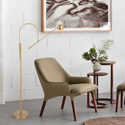 Decorbites modern black metal floor lamp with unique linear capsule arch design next to olive-green upholstered armchair 110v-120v