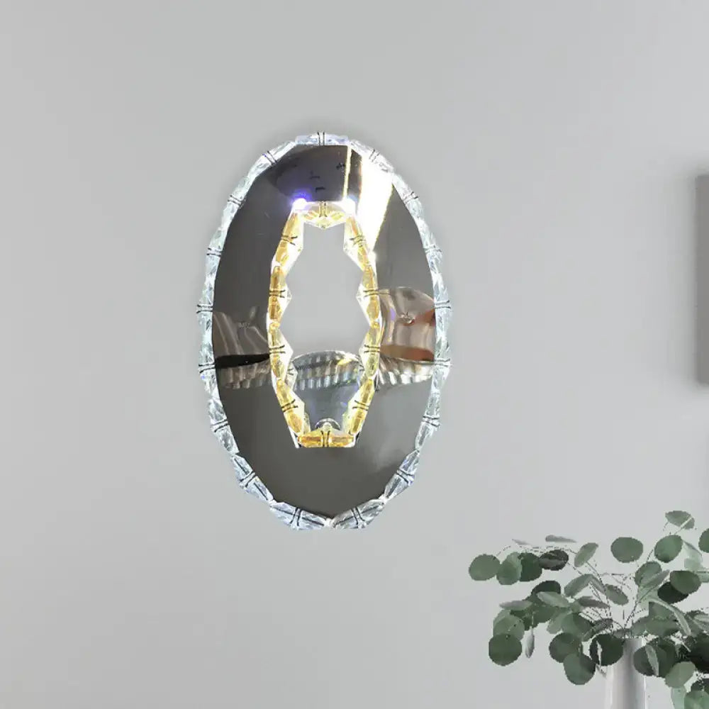 Modern oval chrome crystal wall sconce with sparkling frame and illuminated gold tone detail in warm white light