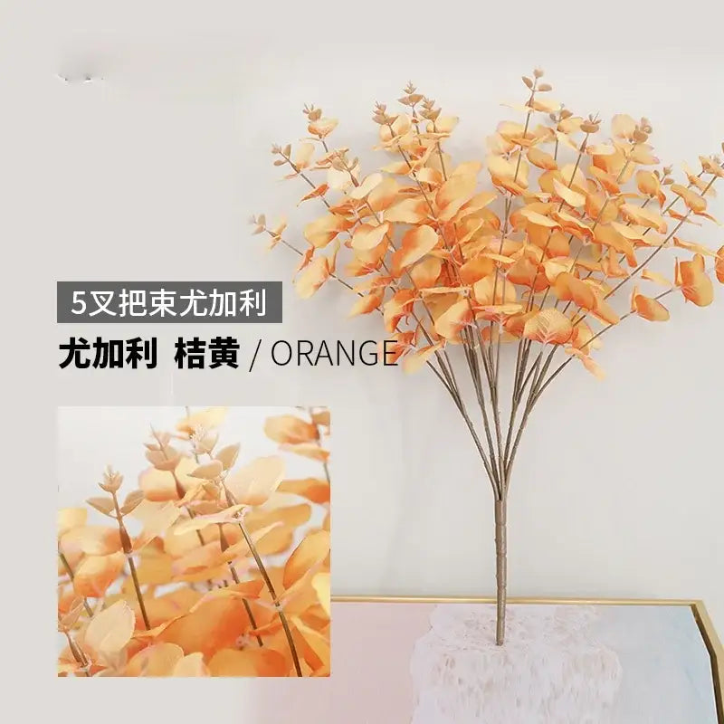 Modern pink eucalyptus flower arrangement with orange artificial eucalyptus flowers and slender stems in a glass vase
