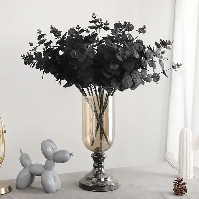 Elegant black eucalyptus flower arrangement in a tall clear glass vase with metallic base for modern living room decor