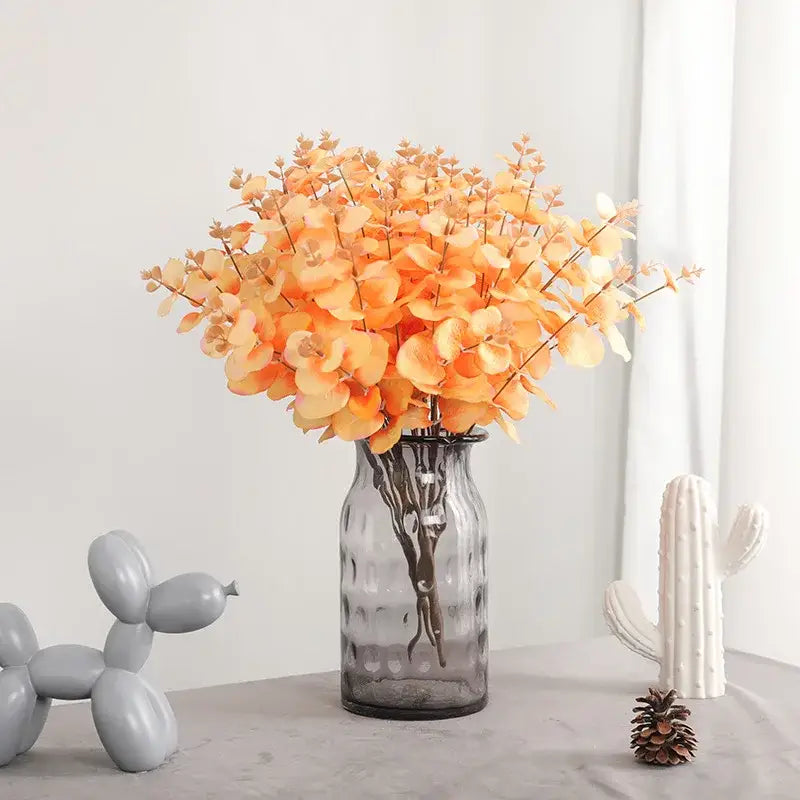 A clear textured glass vase holding a vibrant orange eucalyptus flower arrangement for living room decor