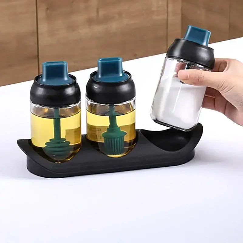 Set of three clear glass seasoning bottles with black and teal lids and green brushes in a modern pink glass set