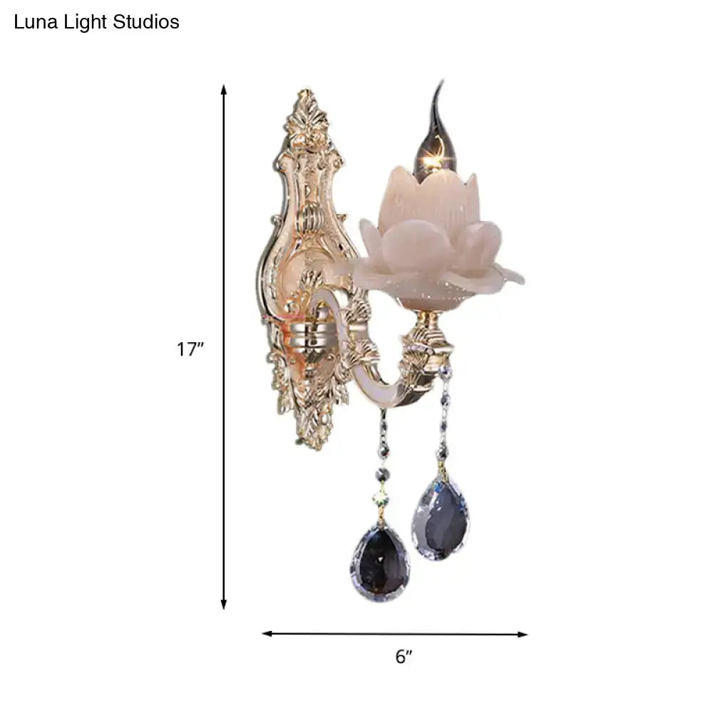 Ornate gold-toned wall lamp with milky glass pink lotus shade and dangling teardrop crystal for bedroom sconce use