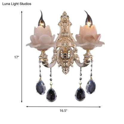 Gold-toned ornate wall lamp with pinkish milky glass lotus shades and dangling dark teardrop crystal accents for bedroom use