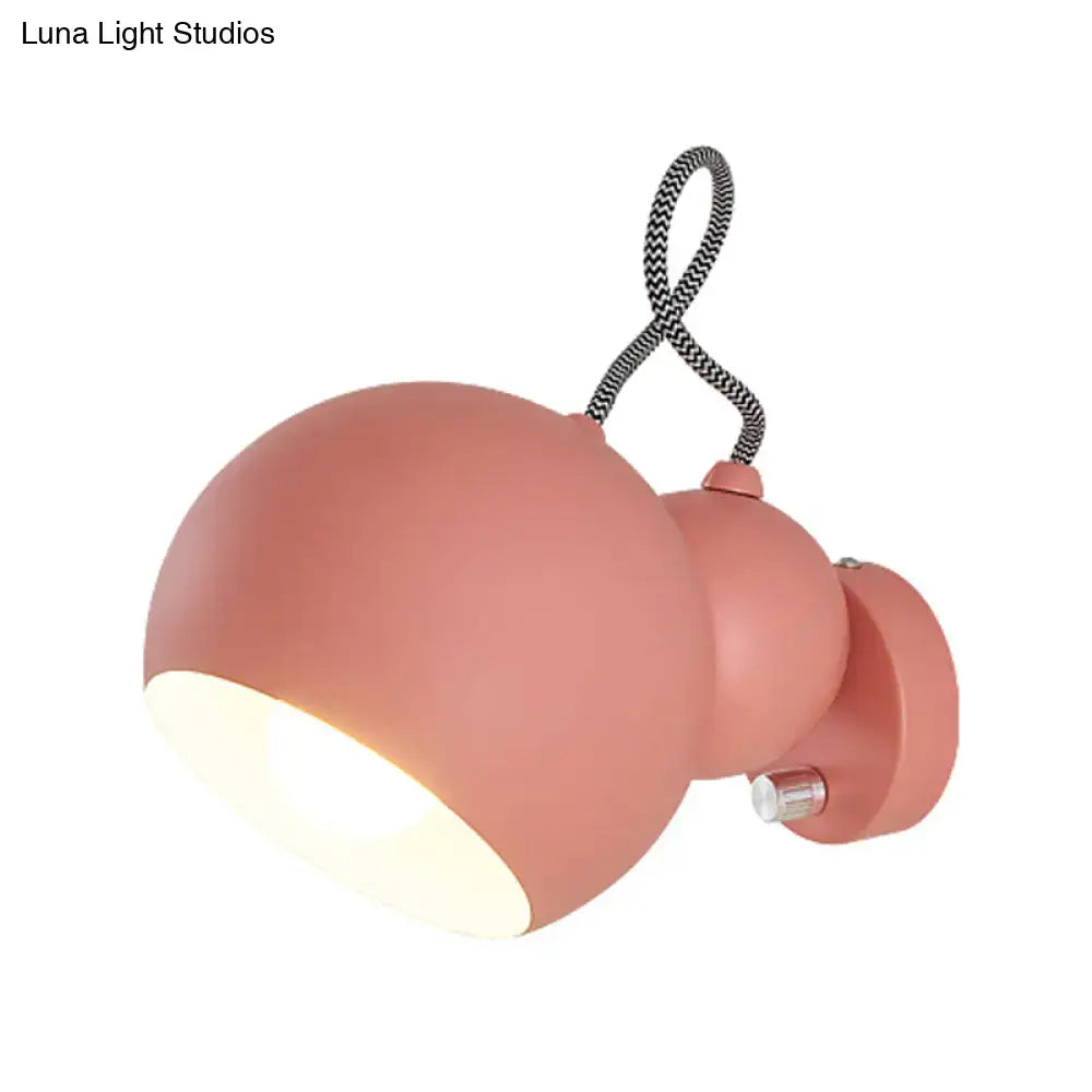 A matte coral-pink wall lamp with an adjustable spherical head and flexible black-and-white braided cord for living room