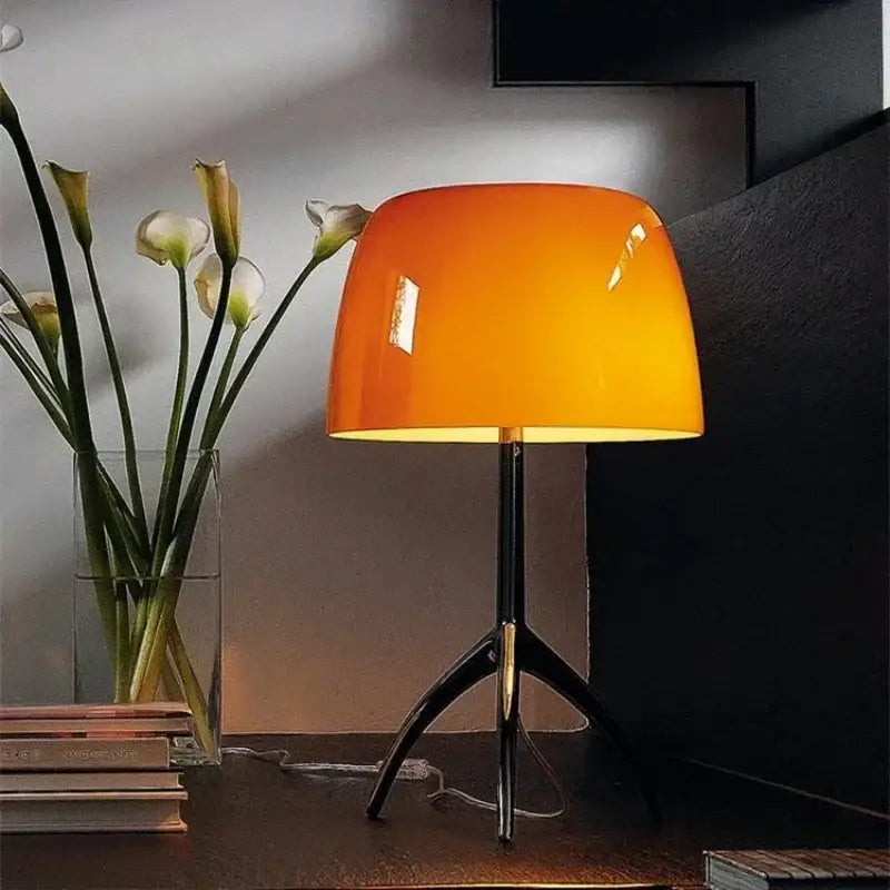 Modern glass shade table lamp with vibrant orange glass shade and sleek black tripod base for bedroom use