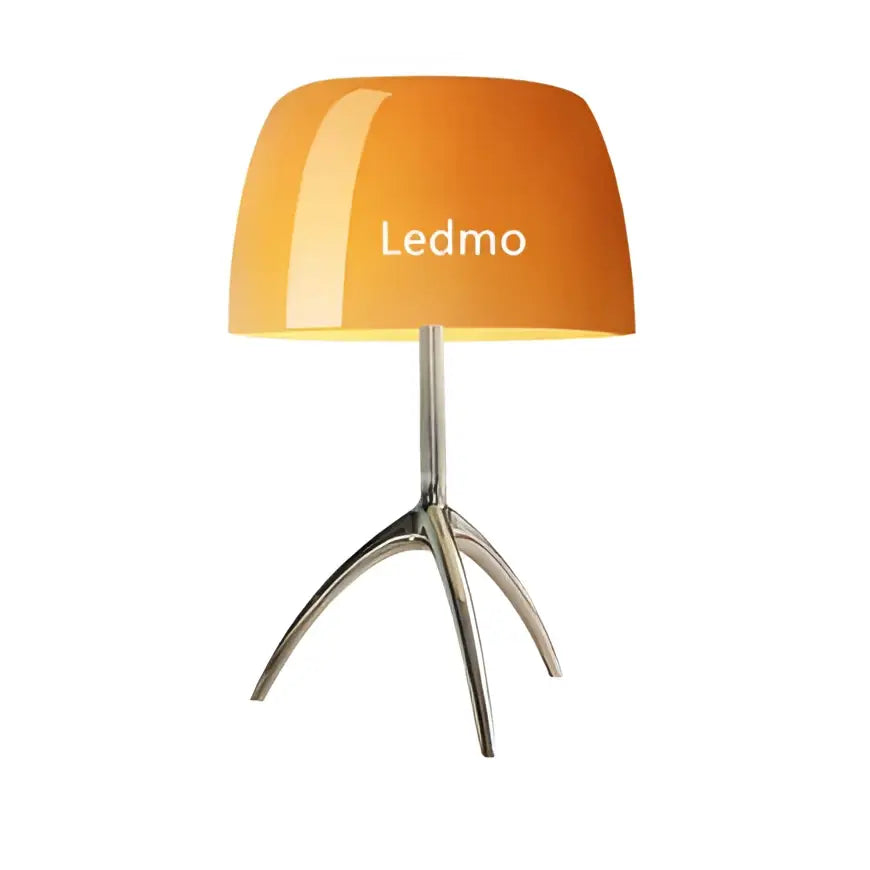 Modern table lamp with orange glossy glass shade and silver metallic tripod base for bedroom use
