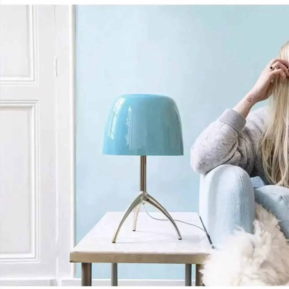Modern table lamp with light blue ceramic base and metallic tripod featuring a glass shade for bedroom use