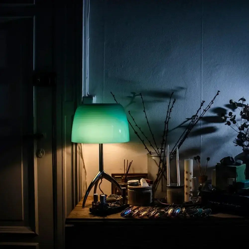 A modern tripod table lamp with a translucent green glass shade emitting a soft glow for bedroom use