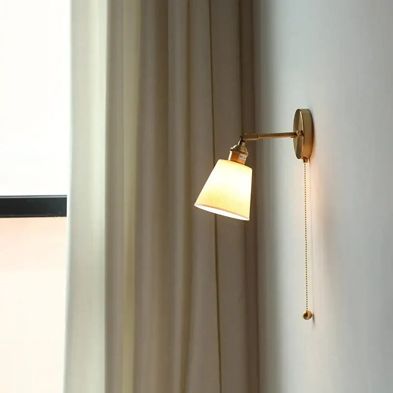A warm-toned brass arm ceramic led wall light with tapered off-white fabric shade for bedroom decorbites ceramic led decor