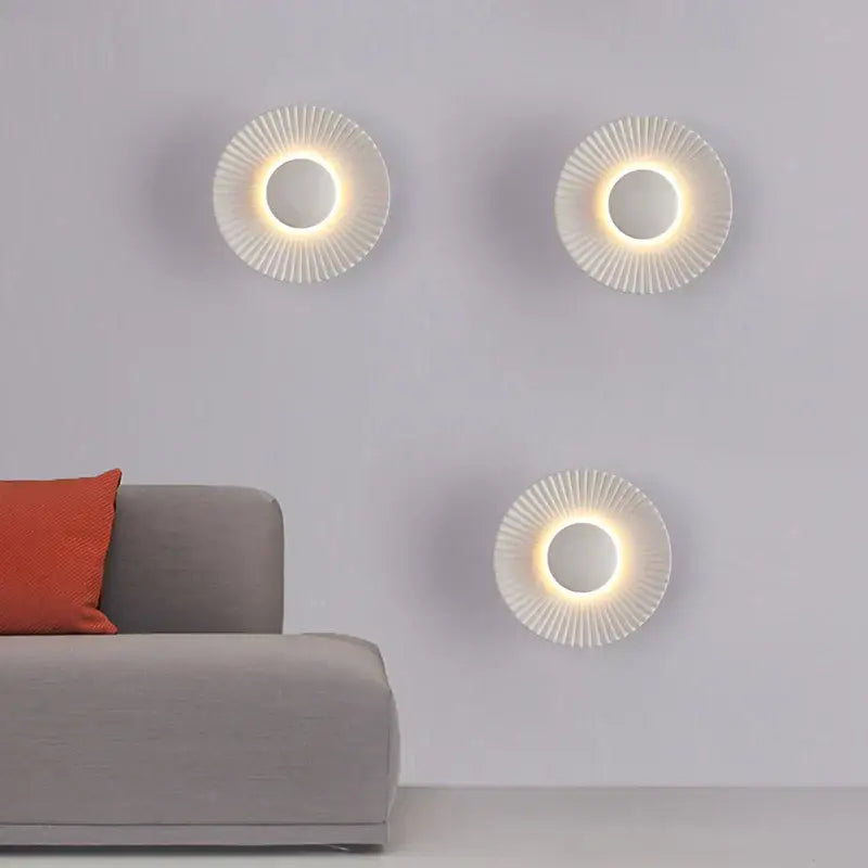 Three modern white and gold led wall lamps with ribbed circular design and warm glowing light for bedroom lighting