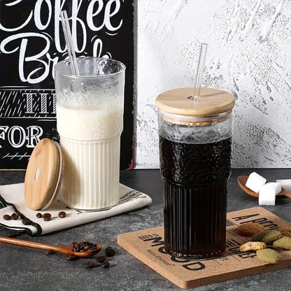 Modern ribbed glass cup with bamboo lid and clear straw filled with dark coffee in a tall ribbed glass tumbler
