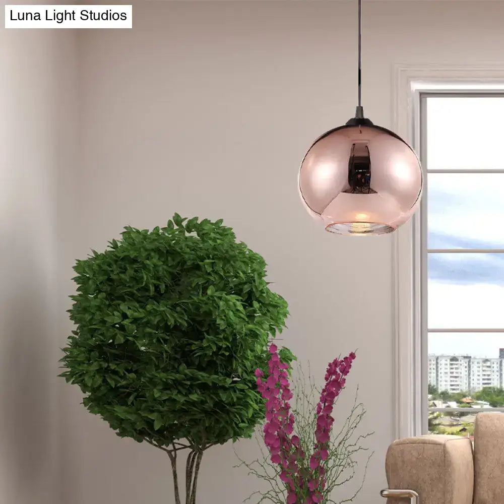 A sleek modern rose gold copper sphere pendant light fixture with reflective glass finish hanging in kitchen bar